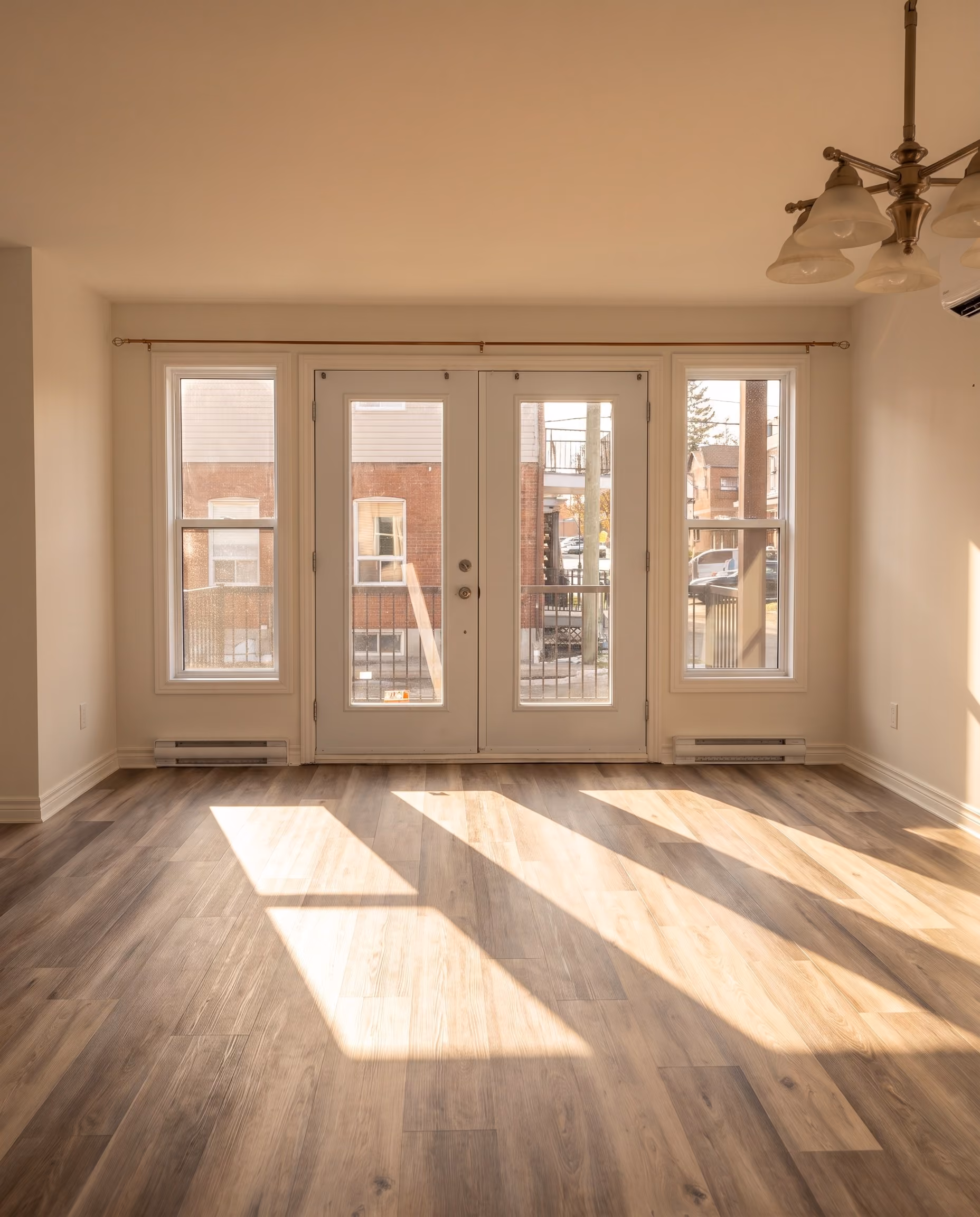 Portes françaises vitrées vues du salon, la lumière du jour dessinant un rectangle sur le plancher de bois.