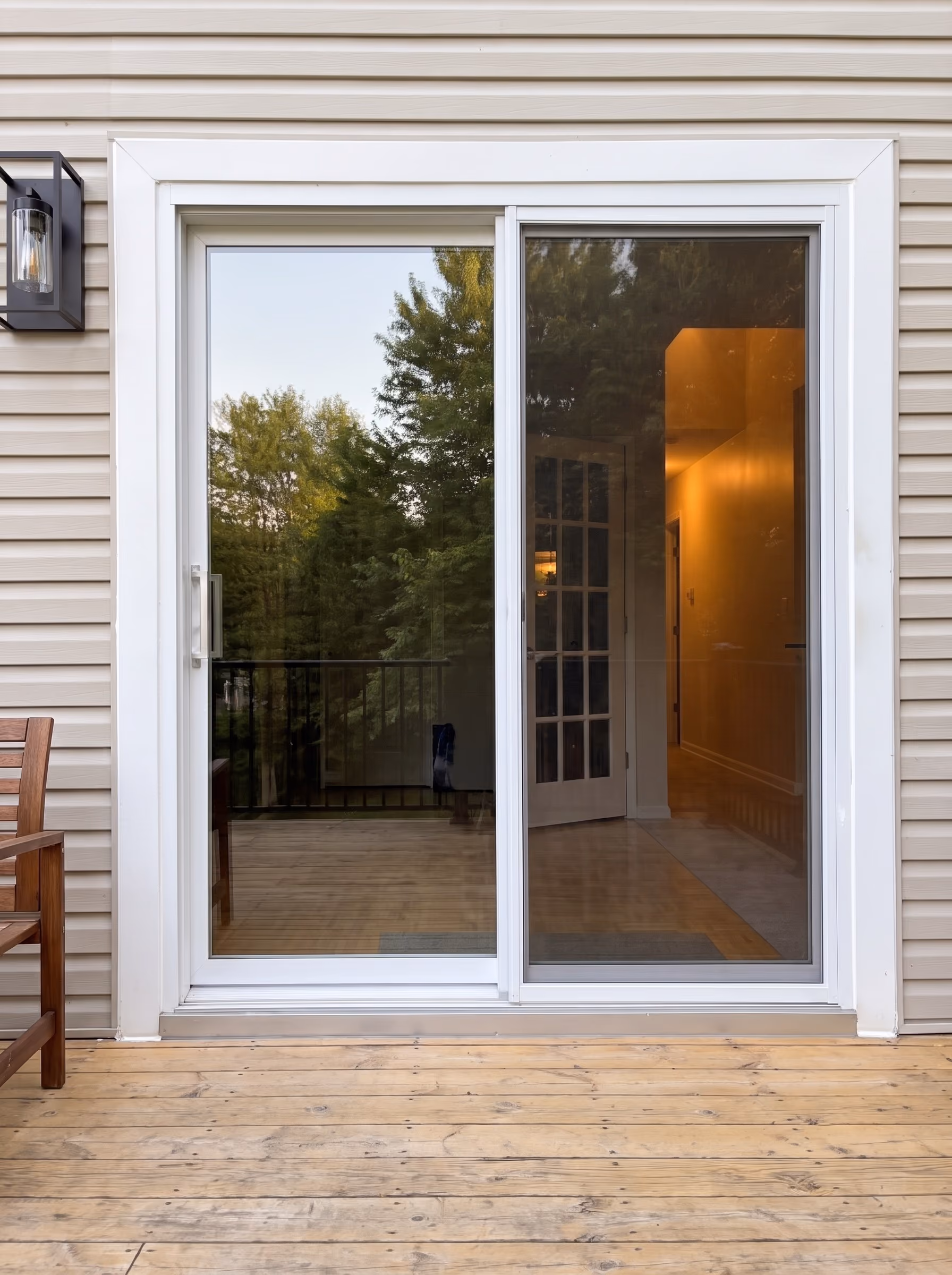 Porte patio coulissante à cadre blanc sur une terrasse de bois, l’intérieur éclairé au travers du verre.